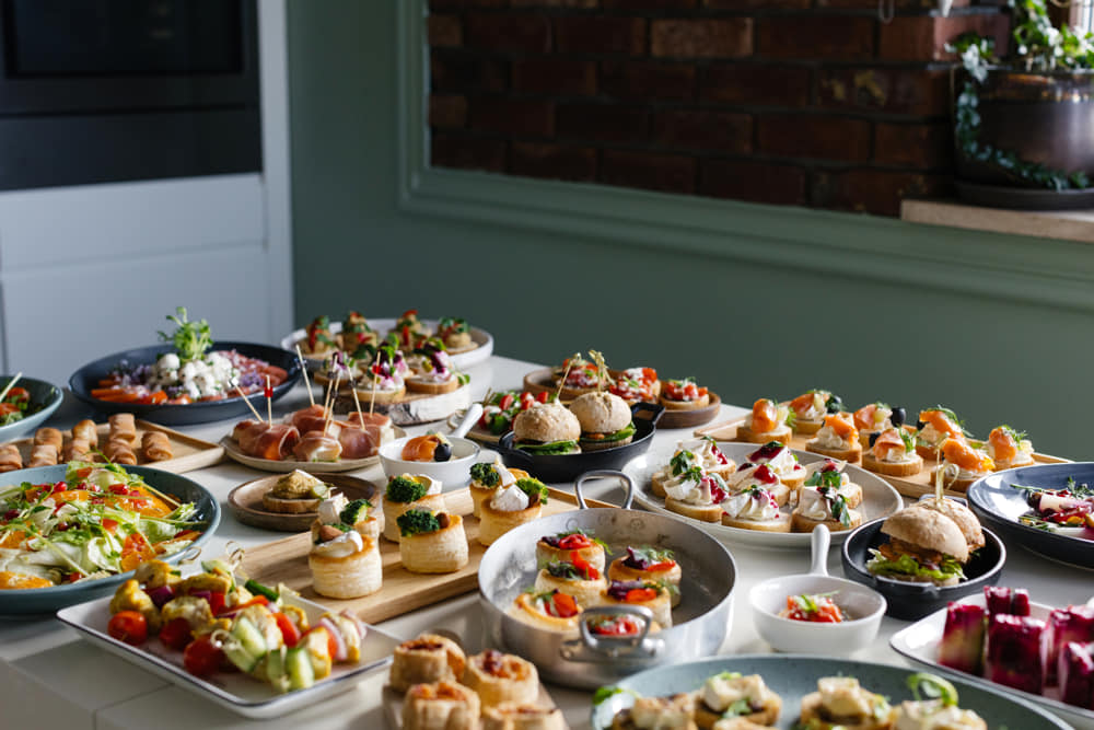 Bufet cateringowy firmowy by Jelonek — długi stół z kilkudziesięcioma przekąskami: canape, tartaletki, sałatki, dania rybne i mięsne, podane na konferencji w biurze